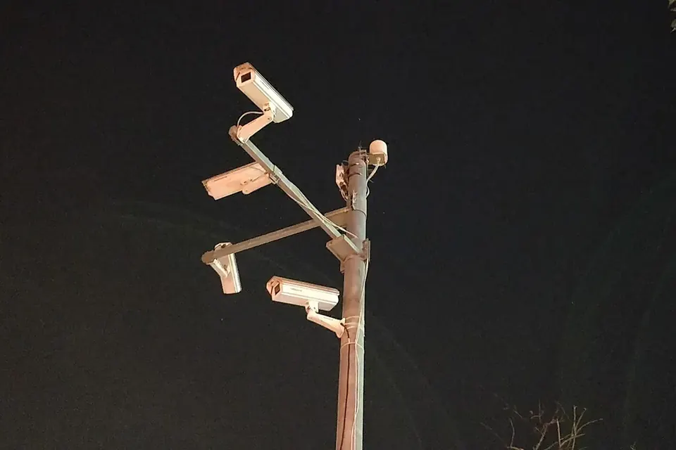 A metal pole at night carrying several white surveillance cameras pointing in different directions