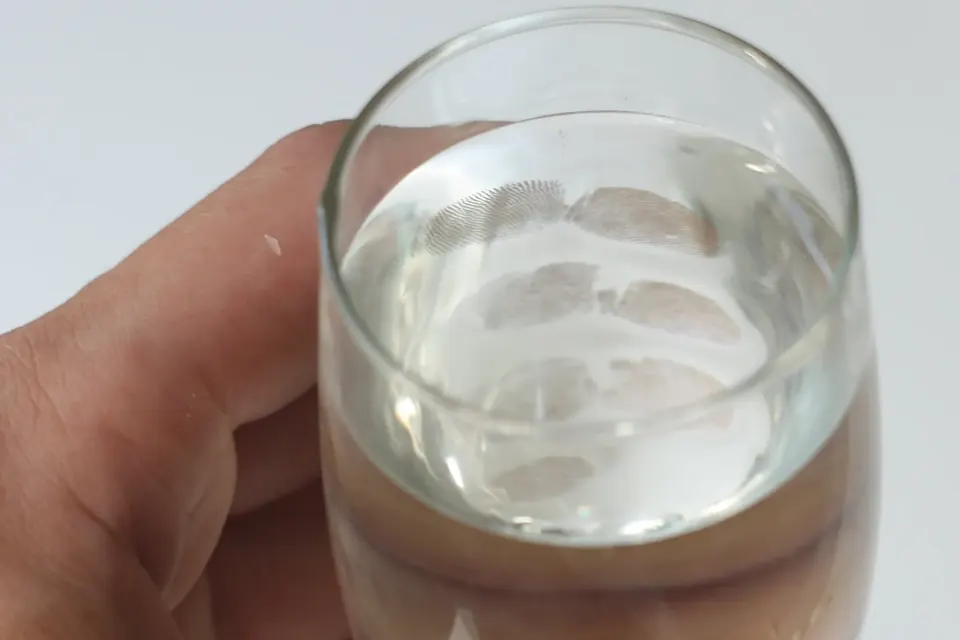 A hand holding a glass of water, with fingerprints on the far side of the glass made visible as sharp light patterns